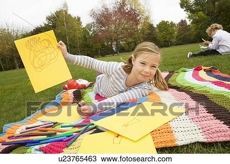 Stock Image - Girl drawing on picnic blanket. Fotosearch