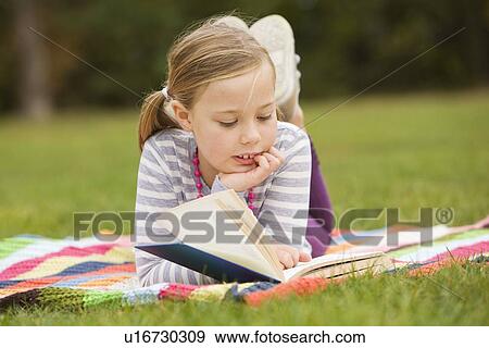 Stock Photo - Girl reading book on picnic blanket. Fotosearch