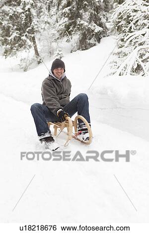 Stock Photograph - Man sitting on sled in snowy field. Fotosearch