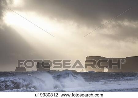 Stock Image - Silhouette of cliffs on stormy beach. Fotosearch