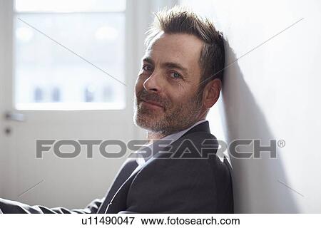 Stock Photo - Smiling businessman sitting in office. Fotosearch