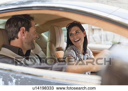 Stock Image - Smiling couple talking in sports car. Fotosearch