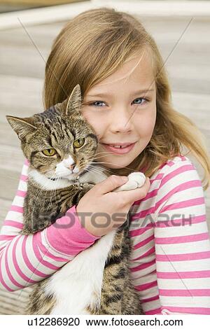 Stock Image - Smiling girl holding cat outdoors. Fotosearch