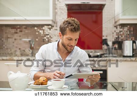 Stock Image - Smiling man reading at breakfast. Fotosearch