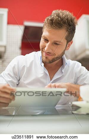 Stock Image - Smiling man reading at table. Fotosearch