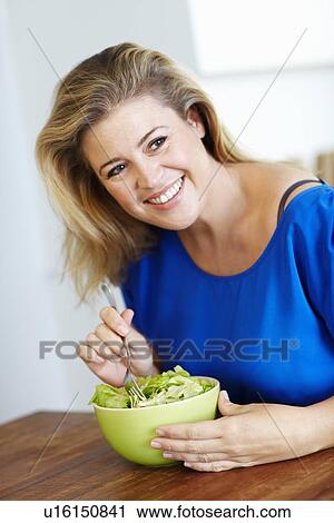 Stock Image - Smiling woman eating salad at table. Fotosearch