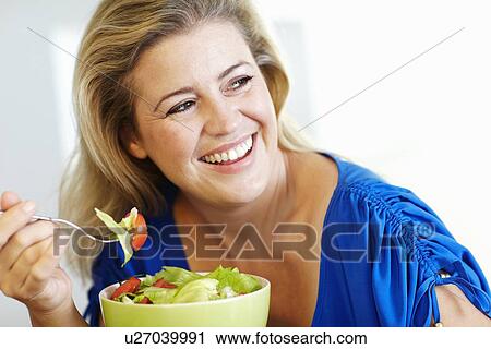 Stock Image - Smiling woman eating salad at table. Fotosearch