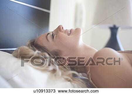 Stock Image - Smiling woman laying on bed. Fotosearch