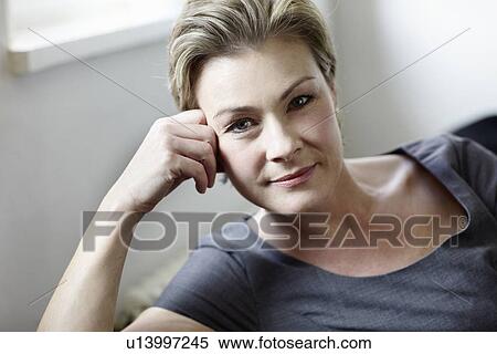 Stock Photography - Smiling woman sitting on sofa. Fotosearch