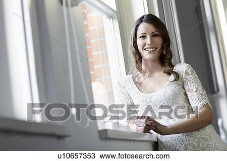 Smiling woman standing at window View Large Photo Image Stock Image - Smiling woman standing at window. Fotosearch