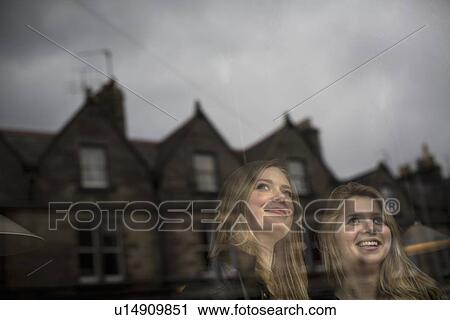 Stock Image - Smiling women standing at window. Fotosearch