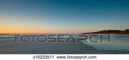 Stock Image - Sun rising over sandy beach. Fotosearch