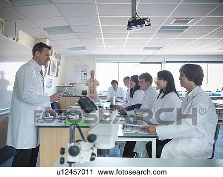 Stock Image - Teacher talking to students in classroom. Fotosearch