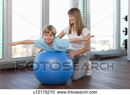 Stock Image - Trainer working with boy in gym. Fotosearch