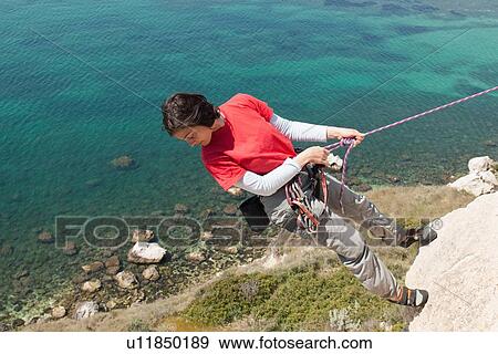 Woman climbing rocky coastal cliff View Large Photo Image Stock Photo - Woman climbing rocky coastal cliff. Fotosearch