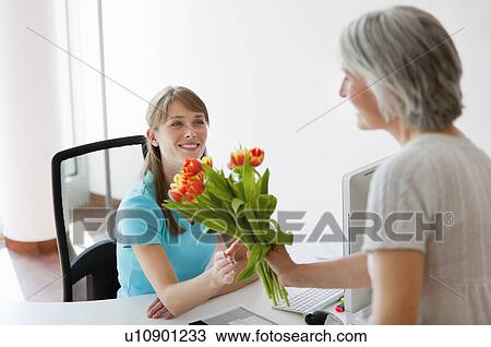 Stock Image - Woman handing receptionist flowers. Fotosearch