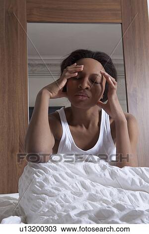 Stock Image - Woman rubbing her temples in bed. Fotosearch