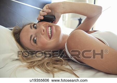 Stock Photograph - Woman talking on cell phone in bed. Fotosearch