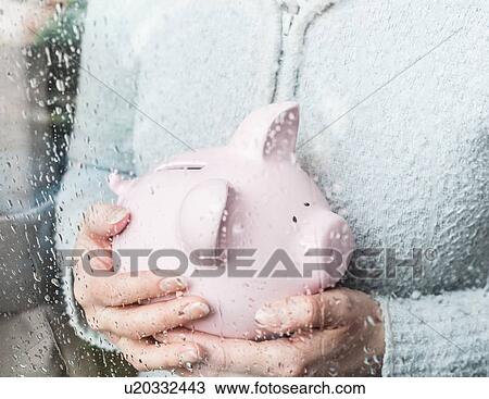 Stock Image - Woman with piggy bank at rainy window. Fotosearch