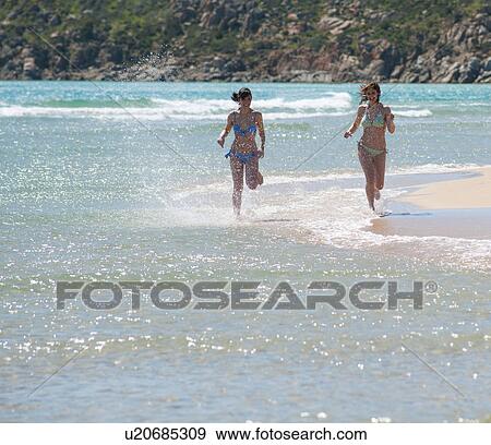 Stock Photo - Women running in waves on beach. Fotosearch