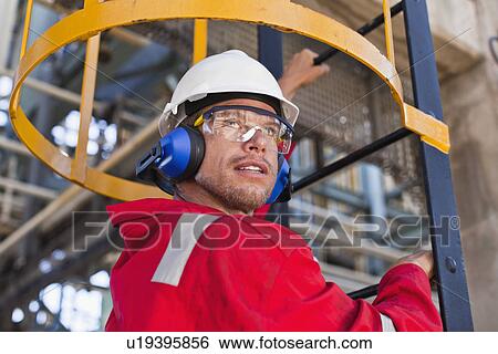 Stock Photograph - Worker climbing ladder at oil refinery. Fotosearch