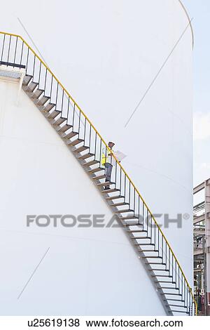 Stock Photo - Worker climbing steps at chemical plant. Fotosearch