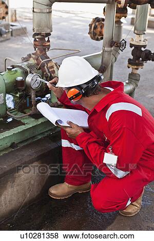 Stock Photo - Worker noting gauge at oil refinery. Fotosearch