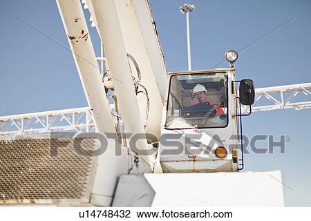 Stock Image - Worker operating crane at oil refinery. Fotosearch