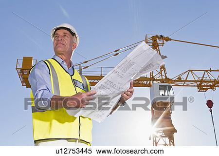Stock Photography - Worker reading blueprints on site. Fotosearch