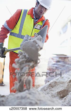 Stock Photo - Worker shoveling concrete on site. Fotosearch