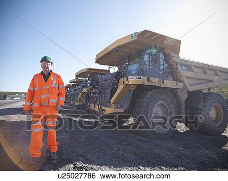 Stock Photograph - Worker standing by trucks at coal mine. Fotosearch