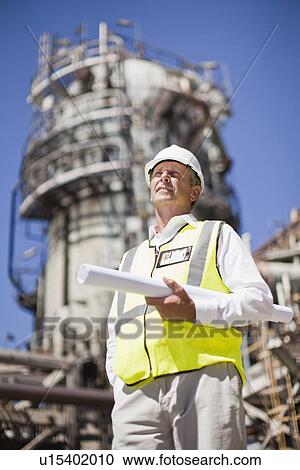 Stock Image - Worker with blueprints at oil refinery. Fotosearch
