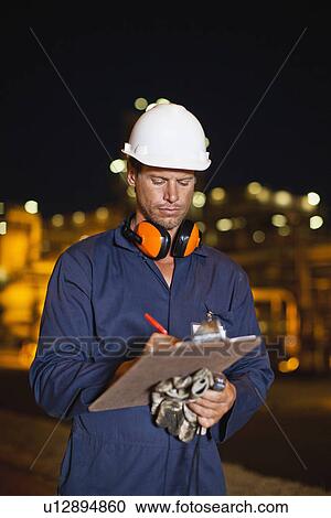 Stock Image - Worker with clipboard at oil refinery. Fotosearch