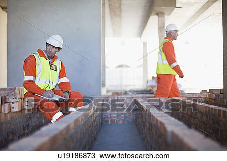 Stock Image - Worker writing on clipboard on site. Fotosearch