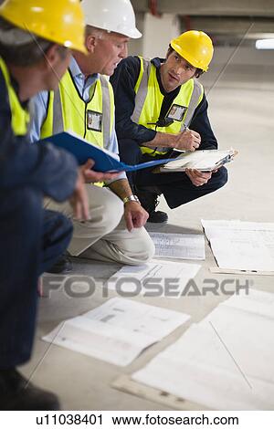 Stock Image - Workers reading blueprints on site. Fotosearch
