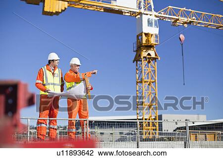 Stock Image - Workers reading blueprints on site. Fotosearch