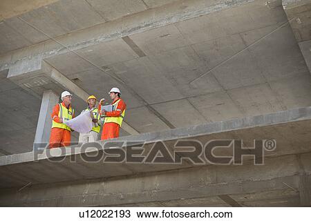 Stock Image - Workers reading blueprints on site. Fotosearch