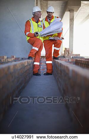 Stock Image - Workers reading blueprints on site. Fotosearch