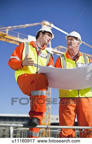 Stock Photo - Workers reading blueprints on site. Fotosearch