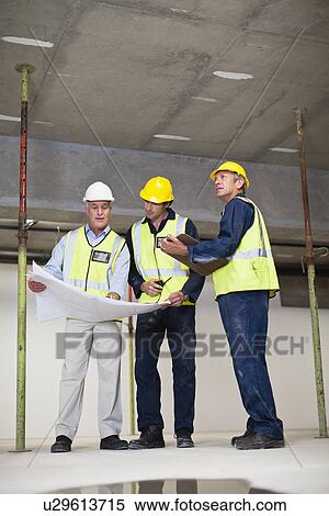 Workers reading blueprints on site View Large Photo Image Stock Photography - Workers reading blueprints on site. Fotosearch
