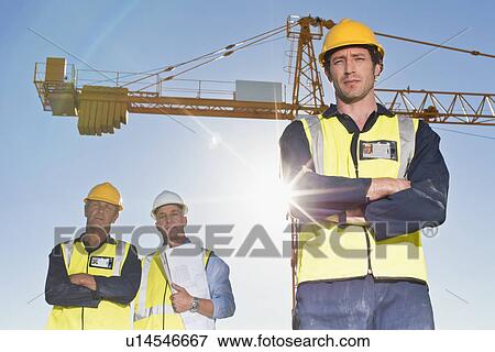 Workers standing at construction site View Large Photo Image Stock Photo - Workers standing at construction site. Fotosearch