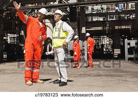 Stock Image - Workers talking at oil refinery. Fotosearch