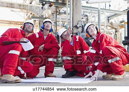 Picture - Workers with blueprints at oil refinery. Fotosearch