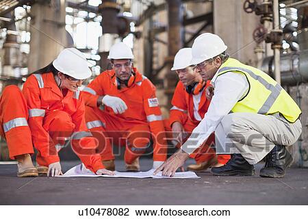 Stock Image - Workers with blueprints at oil refinery. Fotosearch
