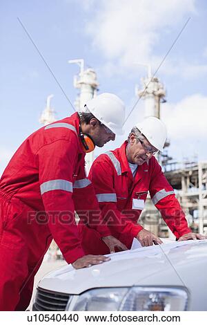 Stock Image - Workers with blueprints at oil refinery. Fotosearch