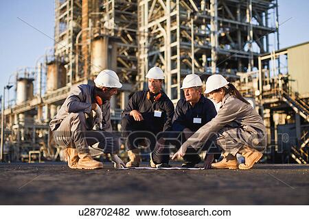 Stock Image - Workers with blueprints at oil refinery. Fotosearch