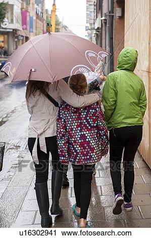 Female friends holding an umbrella in rain on a street, Uppsala, Sweden View Large Photo Image Stock Image - Female friends holding an umbrella in rain on a street, Uppsala, Sweden. Fotosearch