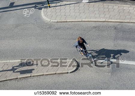 Stock Image - High angle view of a woman cycling on a street, Stockholm, Sweden. Fotosearch