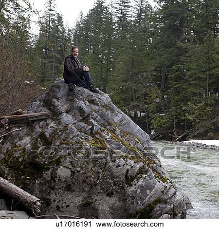 Stock Image - Man relaxing on a rock at the riverside, Nairn Falls Provincial Park, Whistler, British Columbia, Canada. Fotosearch