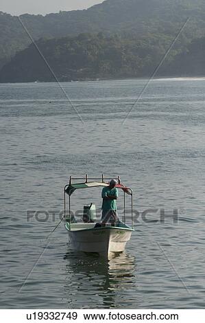 Stock Photo - Man standing on a boat in the sea, Sayulita, Nayarit, Mexico. Fotosearch